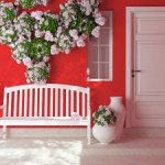Front view of a wooden white door on a red house with window. Beautiful roses and bench on the porch. Exterior of a house.